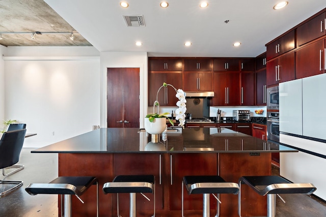 kitchen featuring a breakfast bar, a large island with sink, concrete flooring, and appliances with stainless steel finishes