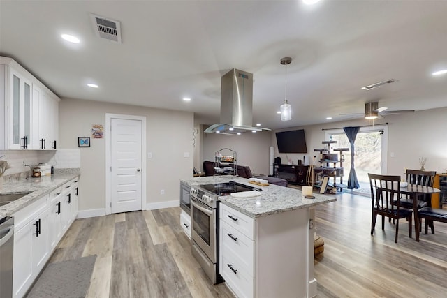 kitchen with stainless steel appliances, island range hood, decorative light fixtures, light hardwood / wood-style flooring, and white cabinets