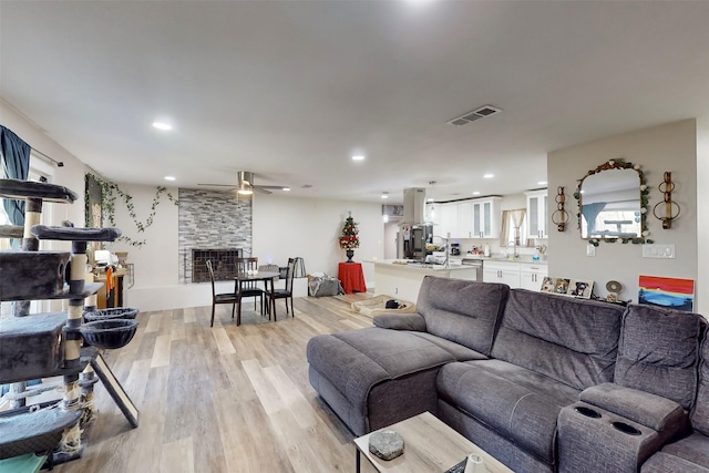 living room with light wood-type flooring, a stone fireplace, and ceiling fan