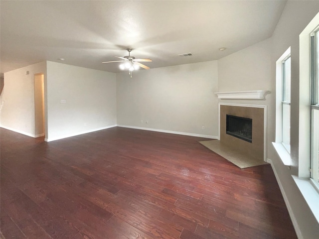 unfurnished living room with a tile fireplace, dark wood-type flooring, and ceiling fan