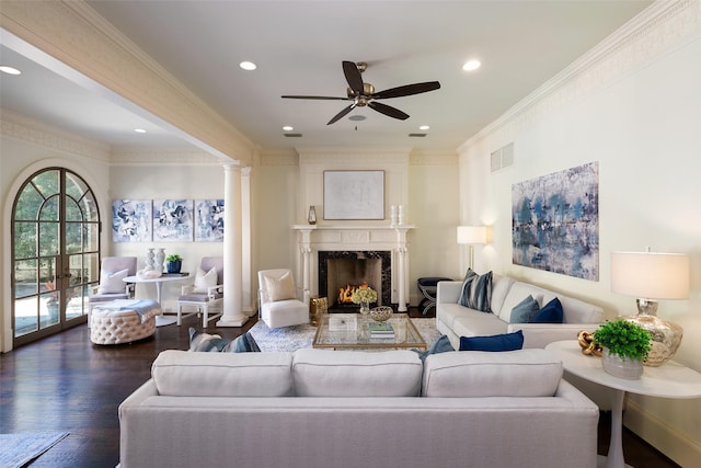 living room featuring ceiling fan, dark hardwood / wood-style flooring, decorative columns, crown molding, and a fireplace