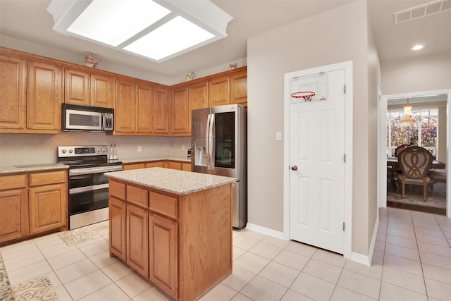 kitchen featuring light stone countertops, appliances with stainless steel finishes, tasteful backsplash, light tile patterned floors, and a kitchen island