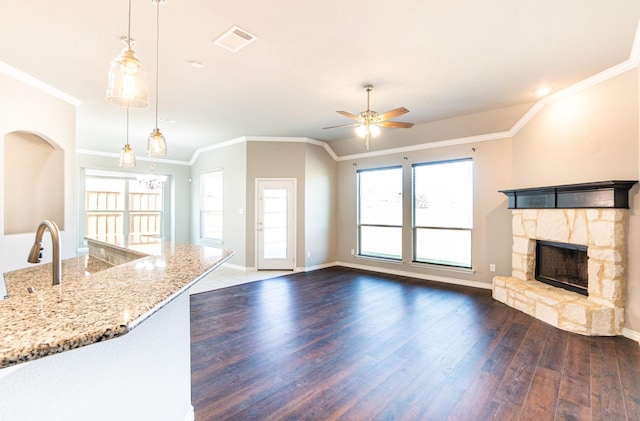 unfurnished living room featuring a stone fireplace, sink, ceiling fan, crown molding, and dark wood-type flooring