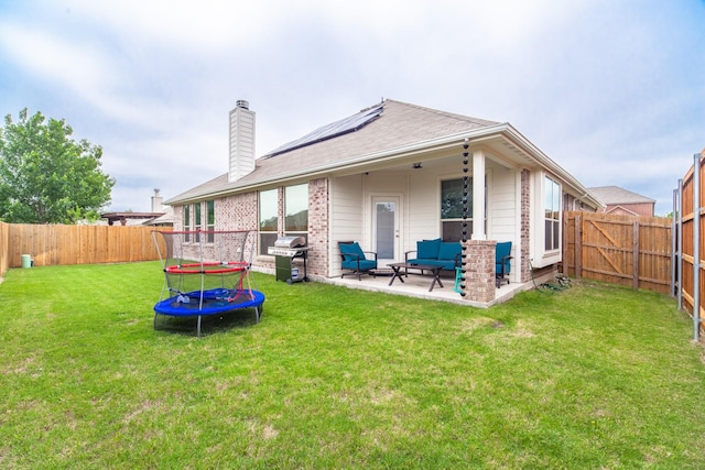 back of property with a lawn, a trampoline, a patio, solar panels, and an outdoor hangout area