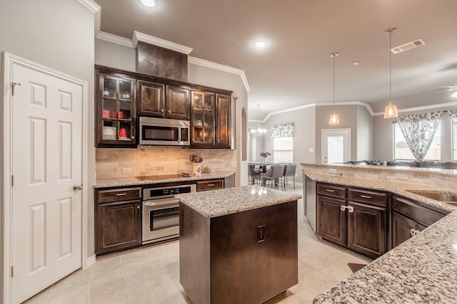 kitchen featuring hanging light fixtures, a center island, light stone counters, stainless steel appliances, and dark brown cabinets