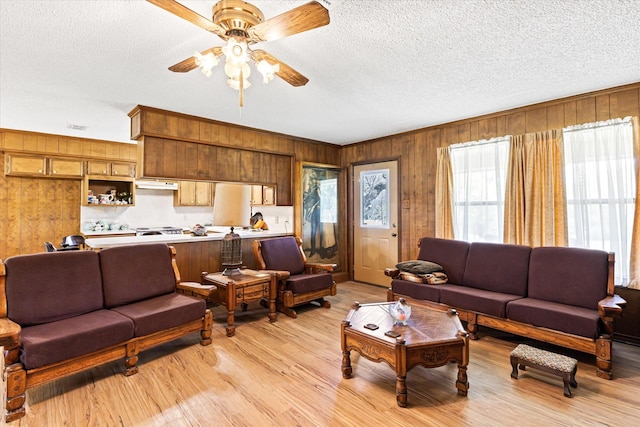 living room featuring wooden walls, light hardwood / wood-style flooring, ceiling fan, and a textured ceiling