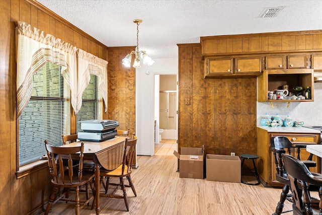 dining room featuring light wood-type flooring, ornamental molding, a textured ceiling, wooden walls, and a chandelier