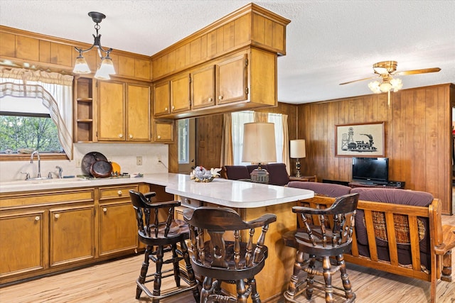 kitchen with pendant lighting, sink, wooden walls, light wood-type flooring, and a kitchen bar