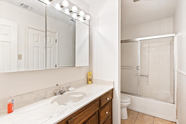 full bathroom featuring shower / bath combination with glass door, tile patterned flooring, vanity, toilet, and a textured ceiling