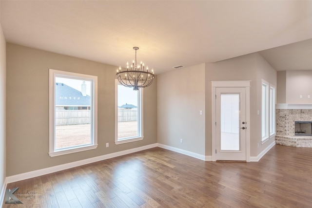 unfurnished dining area featuring hardwood / wood-style flooring, a fireplace, and a notable chandelier