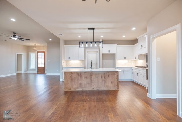 kitchen featuring hardwood / wood-style floors, pendant lighting, white cabinetry, decorative backsplash, and a kitchen island with sink