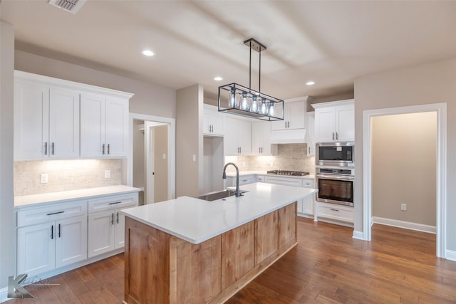 kitchen with white cabinetry, appliances with stainless steel finishes, sink, and a center island with sink