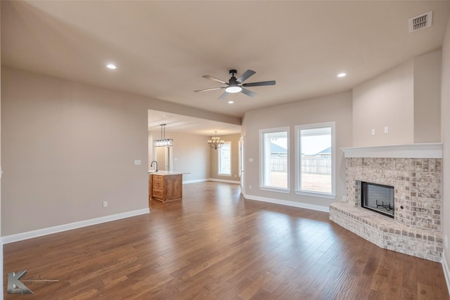 unfurnished living room with a fireplace, dark hardwood / wood-style flooring, and ceiling fan with notable chandelier