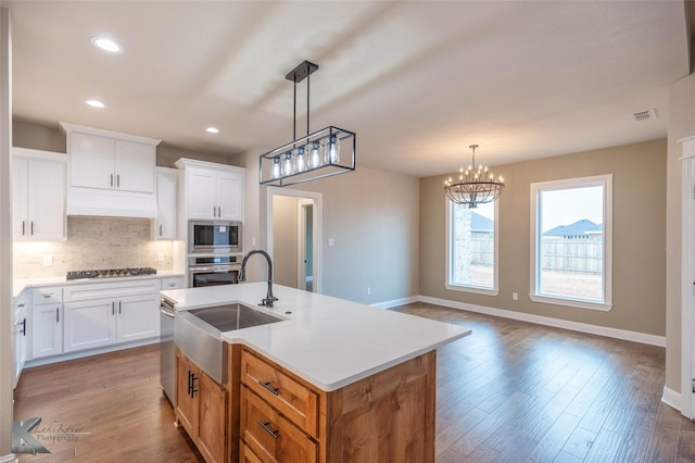 kitchen with white cabinetry, sink, stainless steel appliances, and an island with sink