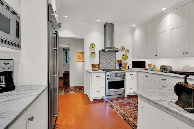 kitchen featuring wall chimney exhaust hood, light stone counters, white cabinetry, and stainless steel appliances