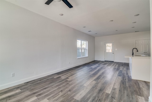 unfurnished living room featuring wood-type flooring, ceiling fan, and sink