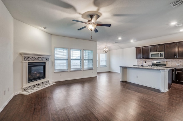 kitchen featuring dark wood-type flooring, stainless steel appliances, an island with sink, decorative backsplash, and dark brown cabinets