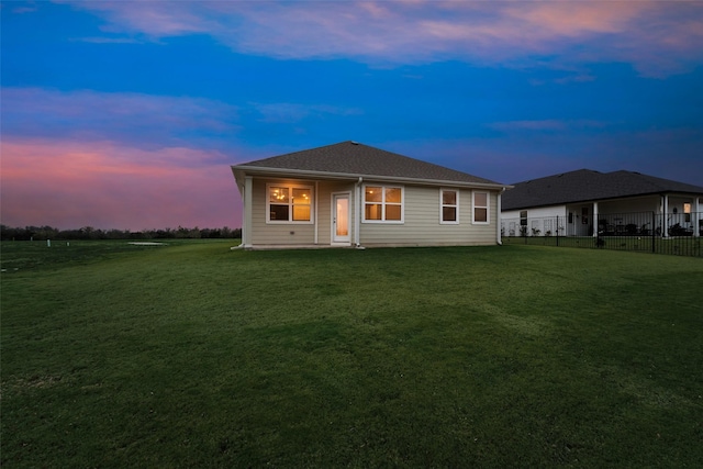 back house at dusk featuring a lawn