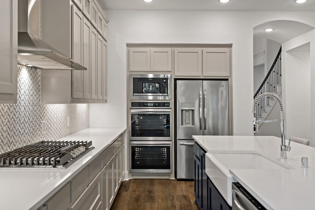 kitchen featuring gray cabinets, dark wood-type flooring, exhaust hood, and appliances with stainless steel finishes