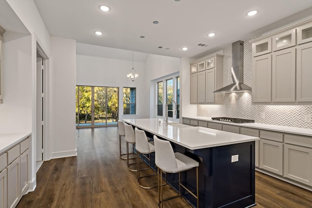 kitchen with sink, wall chimney range hood, dark hardwood / wood-style floors, stainless steel gas stovetop, and a kitchen island with sink