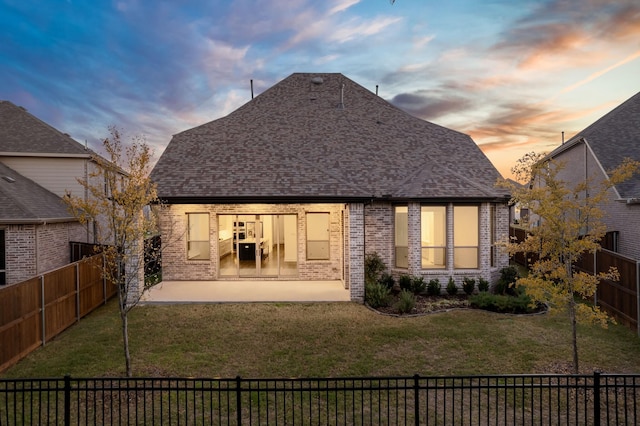 back house at dusk featuring a yard and a patio area