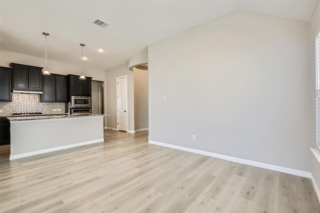 kitchen with light wood-type flooring, tasteful backsplash, stainless steel appliances, decorative light fixtures, and an island with sink