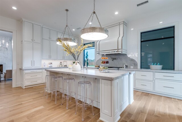 kitchen with white cabinets, an island with sink, tasteful backsplash, decorative light fixtures, and light hardwood / wood-style floors