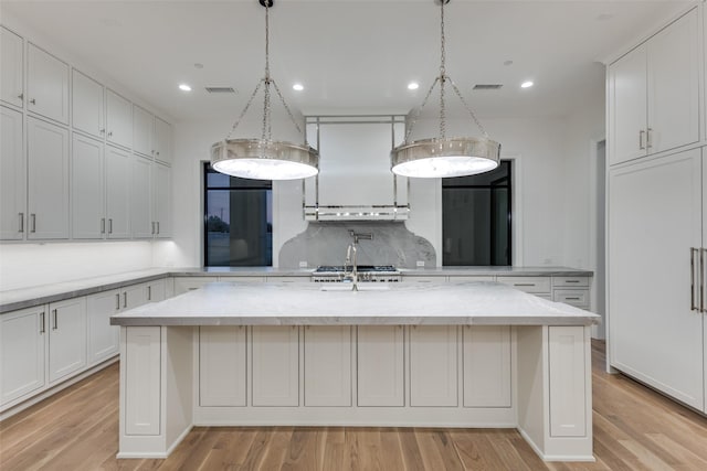 kitchen with decorative backsplash, light stone counters, white cabinetry, and an island with sink