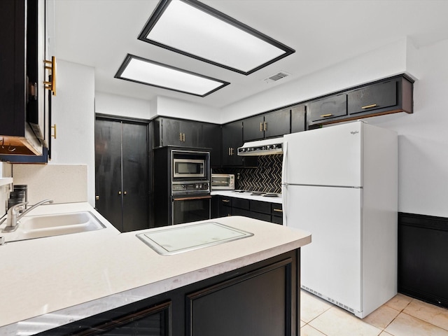 kitchen featuring sink, light tile patterned floors, white refrigerator, black oven, and stainless steel microwave