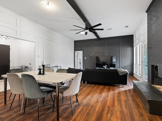 dining space with a fireplace, dark hardwood / wood-style flooring, ceiling fan, and beamed ceiling