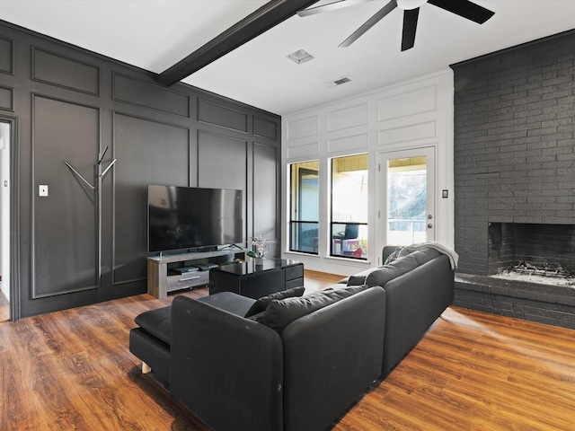 living room with beam ceiling, a brick fireplace, ceiling fan, and hardwood / wood-style flooring