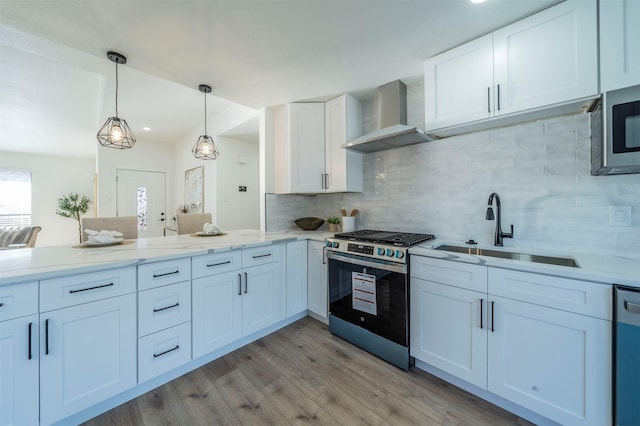 kitchen with white cabinets, appliances with stainless steel finishes, hanging light fixtures, and wall chimney range hood