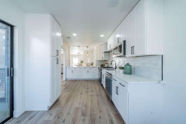 kitchen with white cabinetry, hanging light fixtures, stainless steel appliances, tasteful backsplash, and light hardwood / wood-style flooring