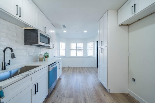 kitchen with sink, white cabinets, light wood-type flooring, and appliances with stainless steel finishes