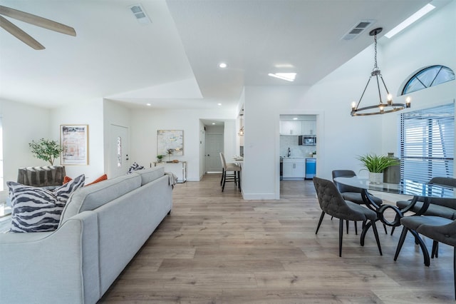 living room with ceiling fan with notable chandelier and light wood-type flooring