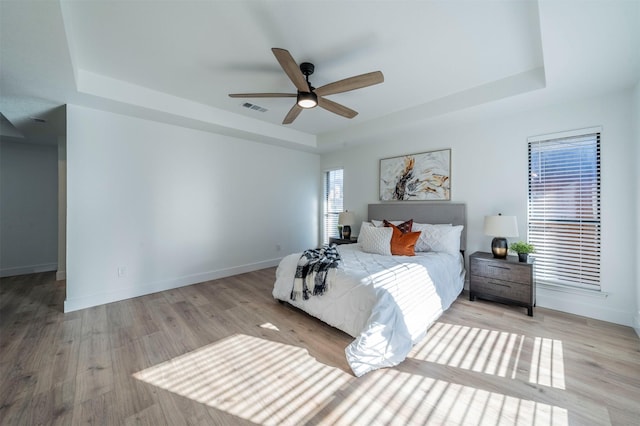 bedroom featuring ceiling fan, a raised ceiling, and light hardwood / wood-style flooring