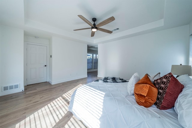 bedroom with light hardwood / wood-style floors, a raised ceiling, and ceiling fan