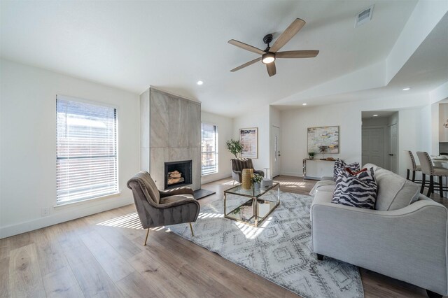 living room featuring a tile fireplace, light wood-type flooring, a wealth of natural light, and ceiling fan