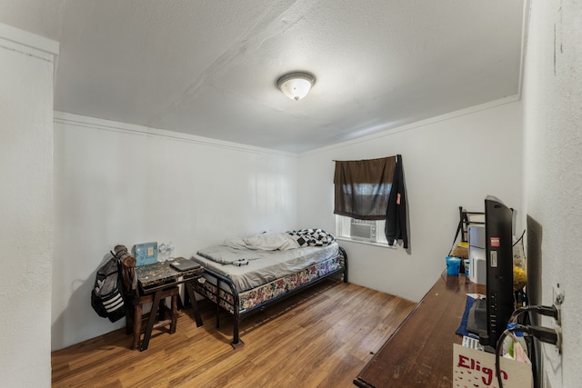 bedroom with crown molding, wood-type flooring, and a textured ceiling