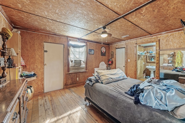 bedroom with hardwood / wood-style flooring, ceiling fan, wood walls, and ensuite bath