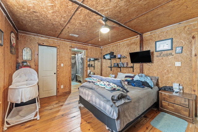 bedroom featuring ceiling fan, wood-type flooring, wooden walls, and ensuite bath