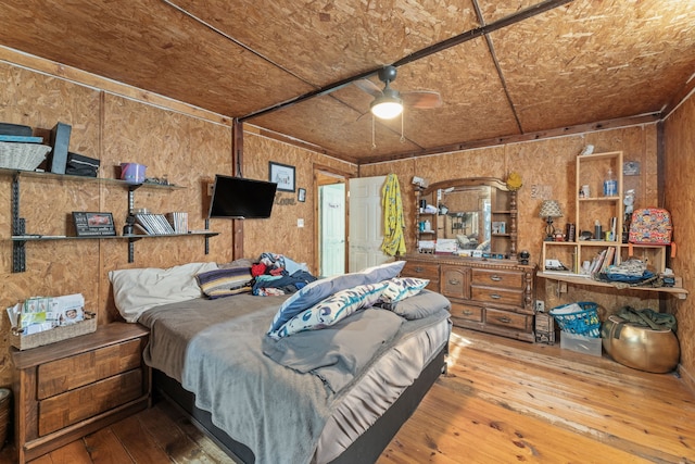 bedroom featuring ceiling fan, wooden walls, and hardwood / wood-style flooring