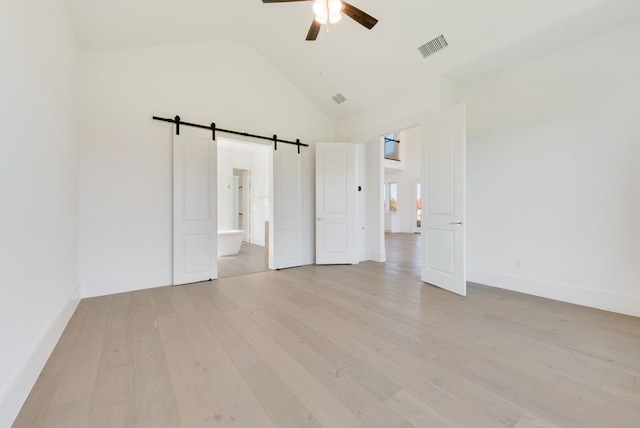 unfurnished bedroom with ensuite bathroom, a barn door, high vaulted ceiling, and light wood-type flooring