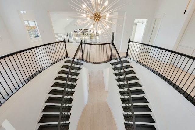 stairs with an inviting chandelier, hardwood / wood-style floors, and a high ceiling