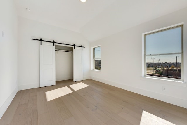 unfurnished bedroom featuring multiple windows, a barn door, lofted ceiling, and light hardwood / wood-style flooring