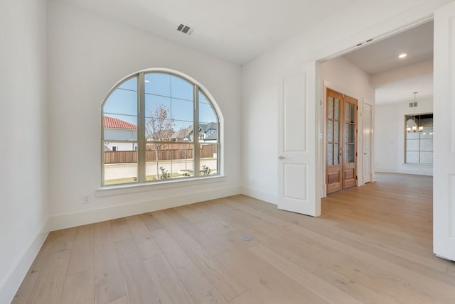 spare room featuring an inviting chandelier and light hardwood / wood-style flooring