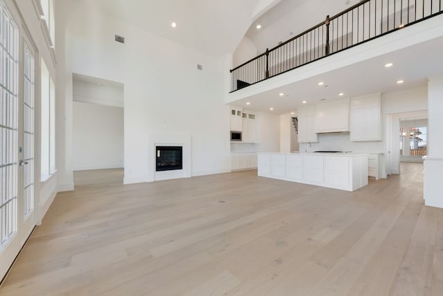 unfurnished living room featuring a towering ceiling, a chandelier, and light hardwood / wood-style floors