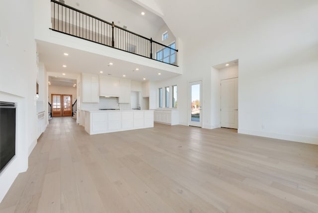 unfurnished living room featuring a multi sided fireplace, a towering ceiling, and light wood-type flooring