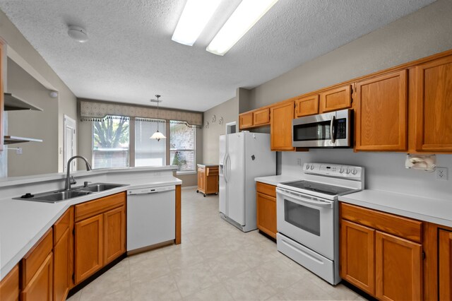 kitchen with a textured ceiling, sink, hanging light fixtures, and white appliances