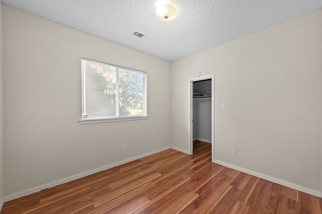 unfurnished bedroom featuring hardwood / wood-style floors, a textured ceiling, a spacious closet, and a closet